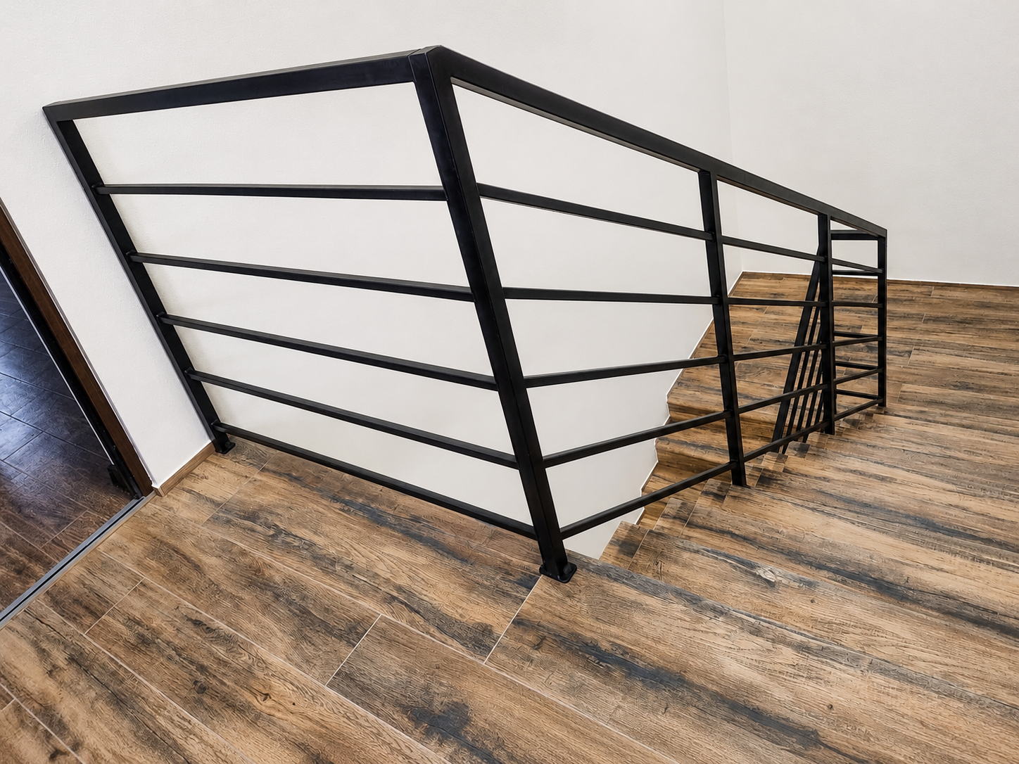 Nowoczesne schody z drewnianymi stopniami i czarną metalową balustradą w minimalistycznym wnętrzu z betonową ścianą i dużymi oknami.