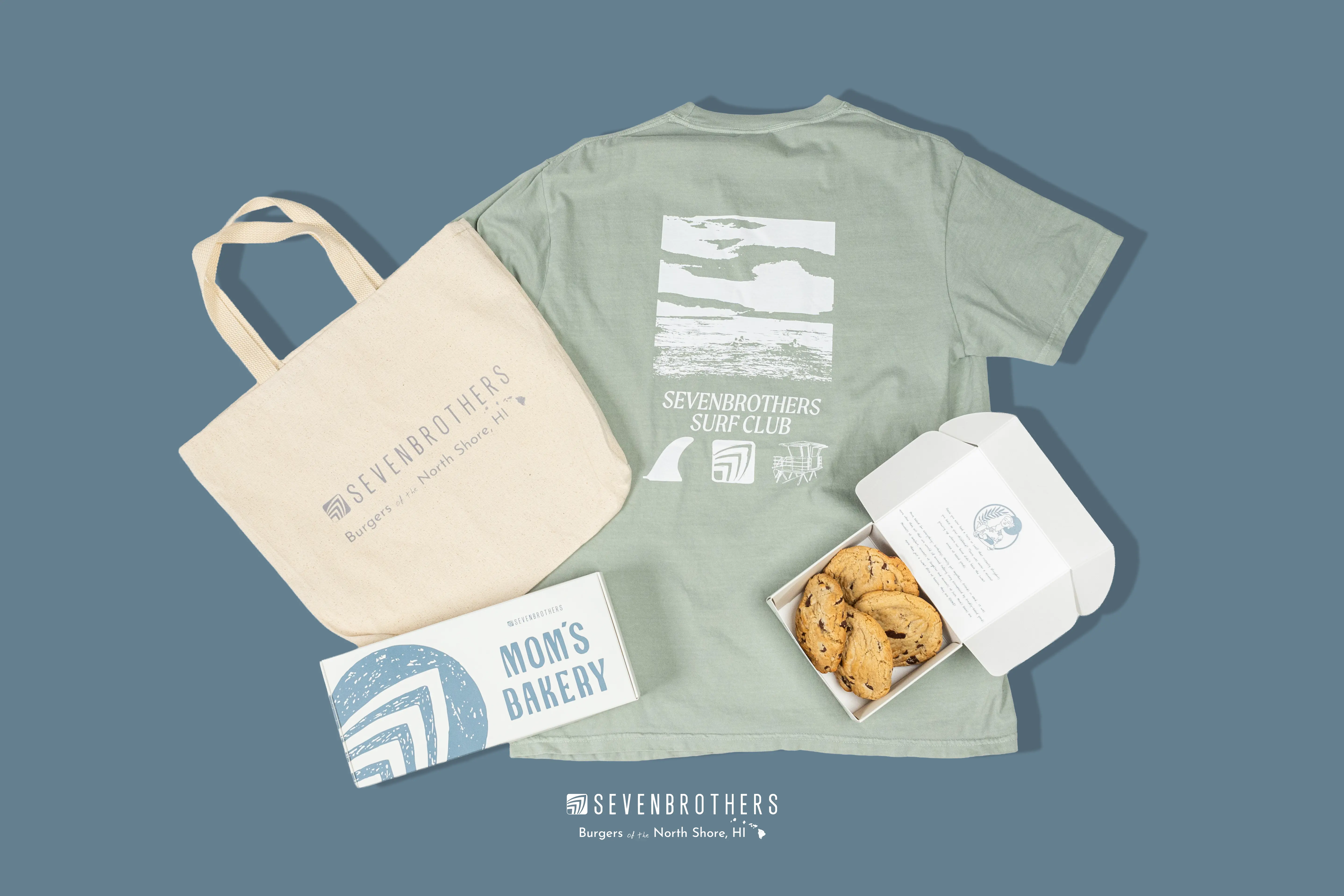 A tshirt, bag, and cardboard carrying case made for Seven Brother's, displayed next to some of their cookies.