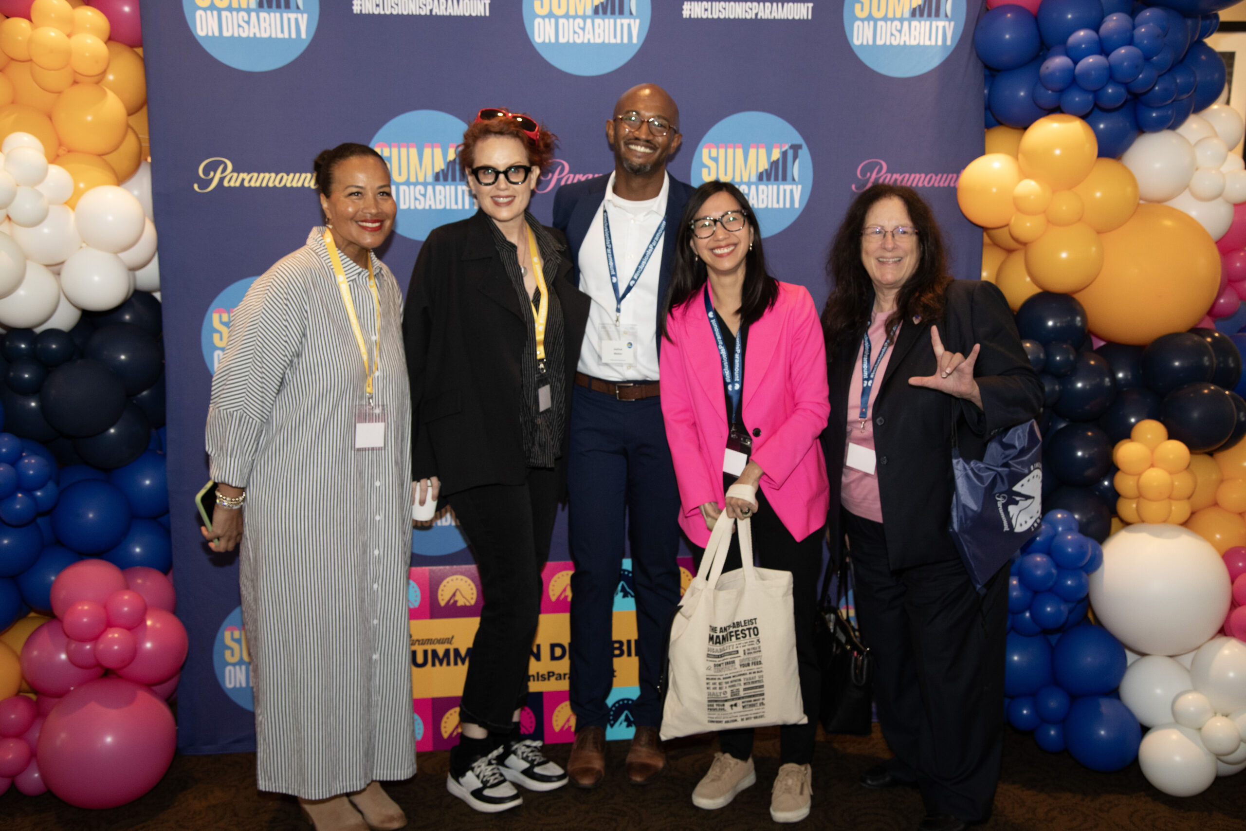 Five individuals smile and pose against a background that reads Paramount Summit on Disability.