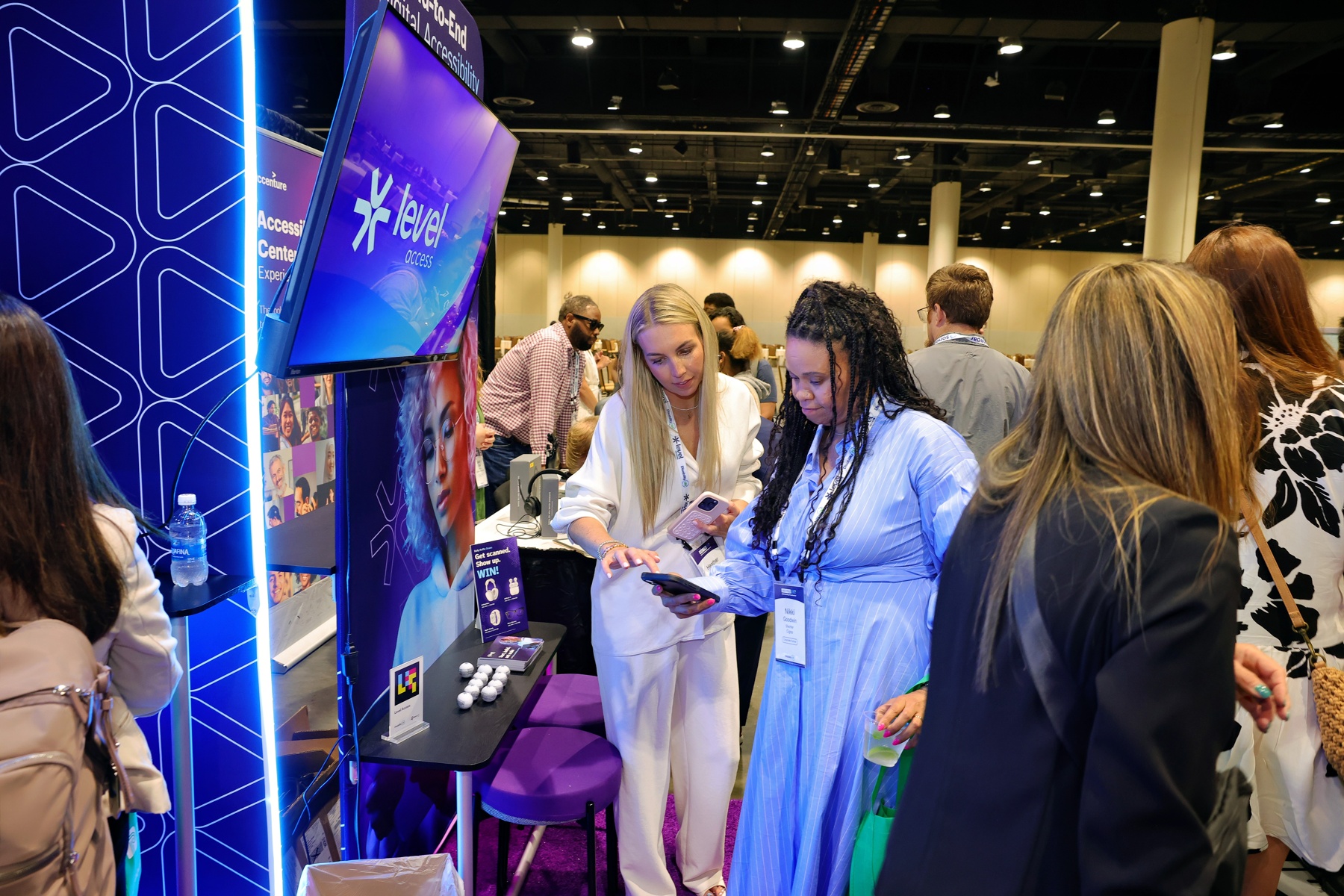 A group of people clustered in the level access booth at the Disability:IN Expo hall. They are demoing the product on the users phone. 