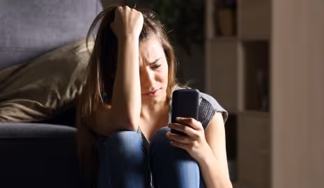 Adolescent aged girl looking stressed while staring at her mobile phone.
