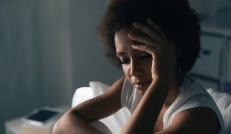 Middle aged African American woman holding her head with a sad expression on her face.