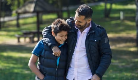 Happy son and father smiling and talking while walking outdoors in a park