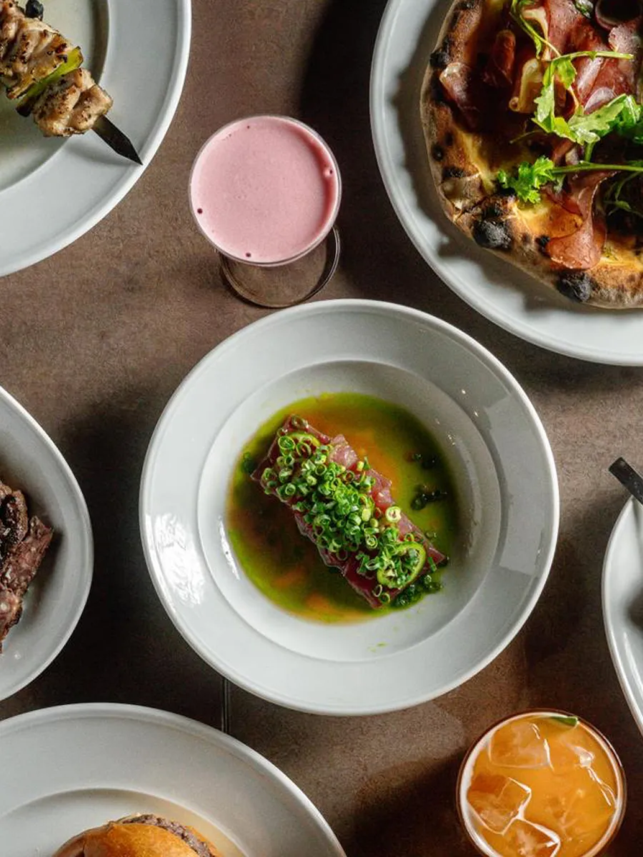 Interior view of a cafe with two people sitting at the counter and empty tables and chairs in the foreground.