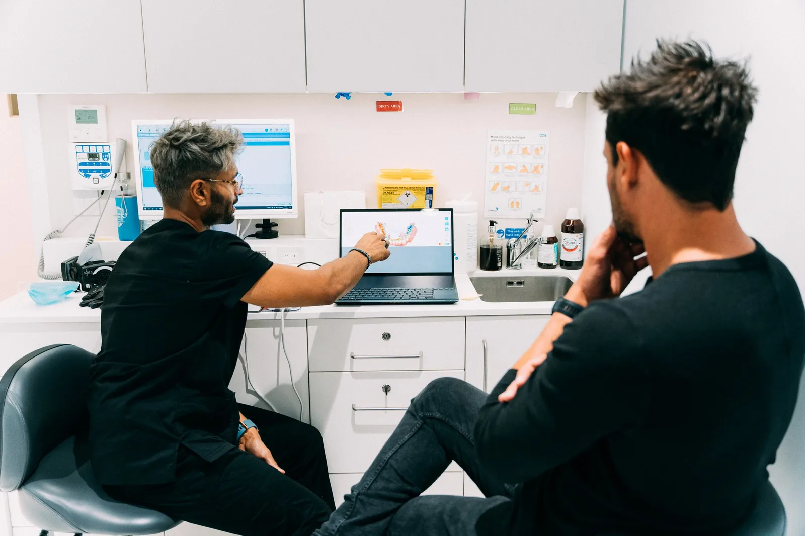 Dentist gesturing at a 3D tooth scan on a laptop while explaining treatment to a patient