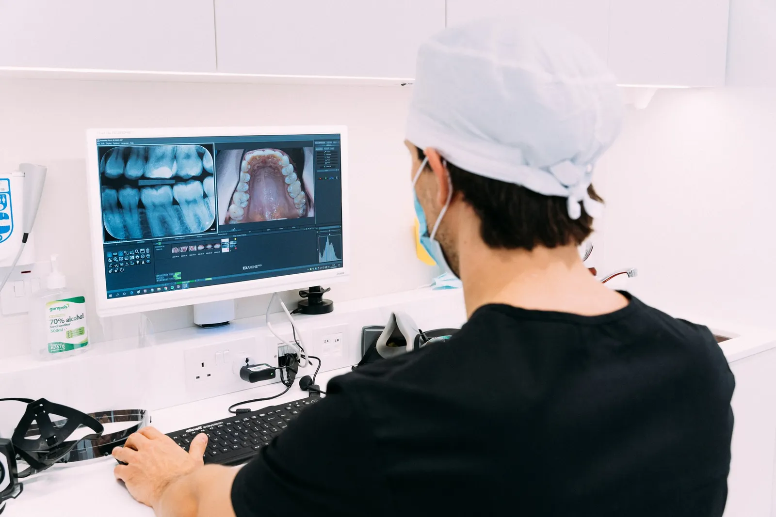 Dentista observa uma radiografia e uma fotografia intraoral lado a lado num monitor da clínica