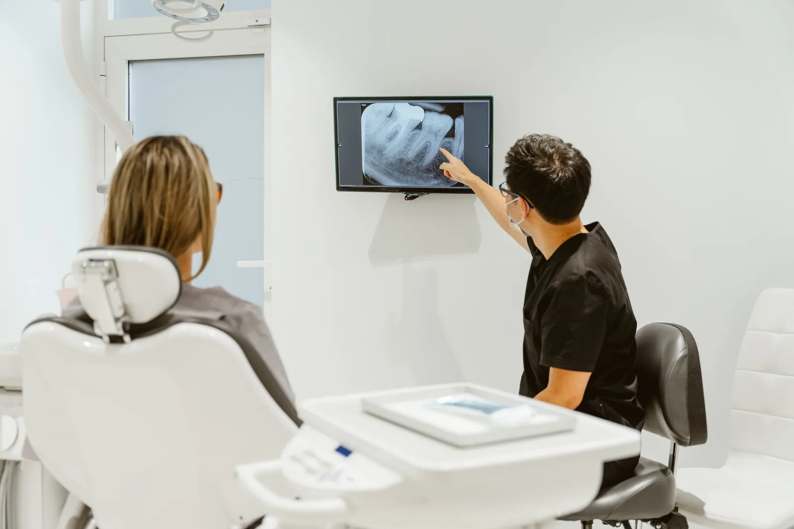 Dentista aponta para uma radiografia dentária no ecrã durante uma consulta detalhada com um paciente