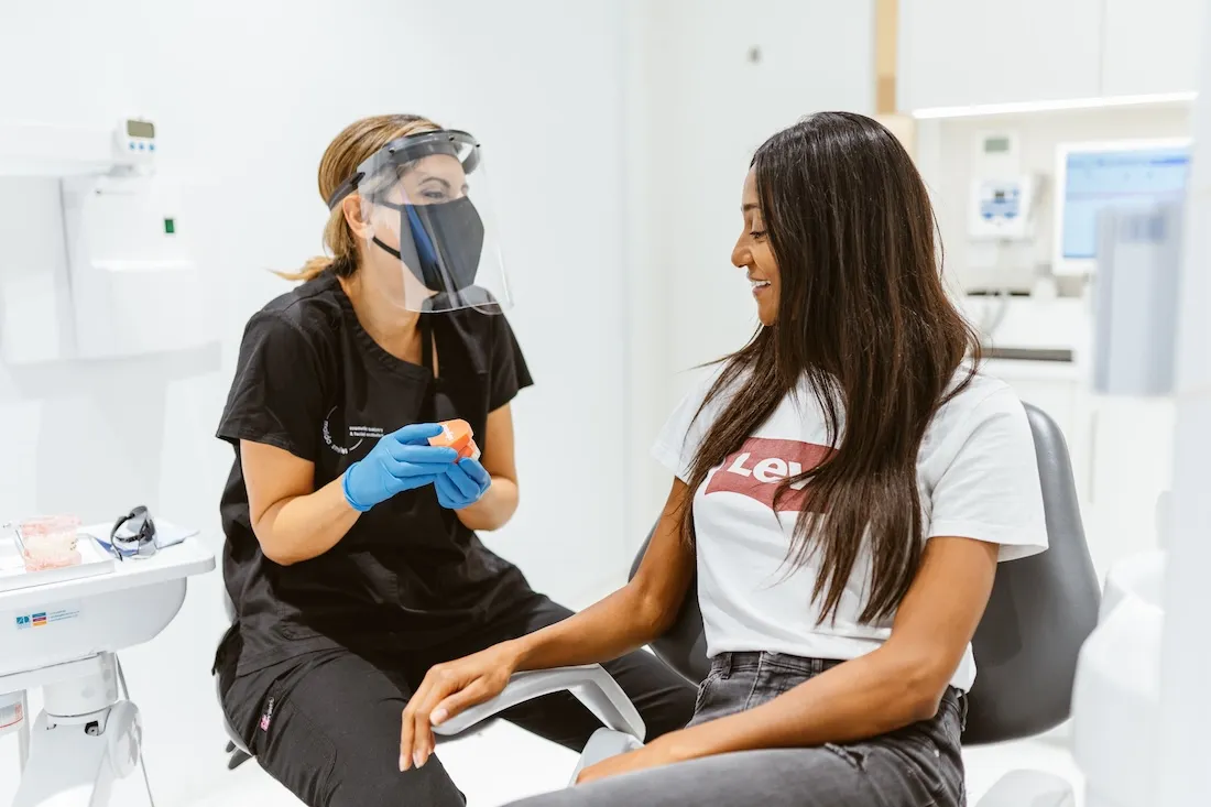 Dental clinician wearing a visor chatting with a patient in the treatment room