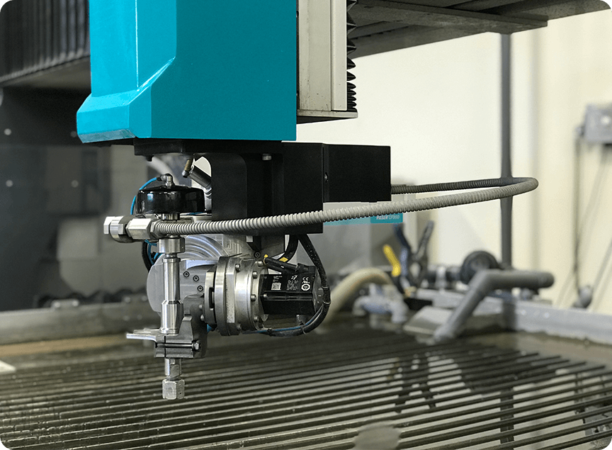 Close-up of a precision waterjet cutting machine nozzle and mechanism over a metal grate bed in an industrial setting.