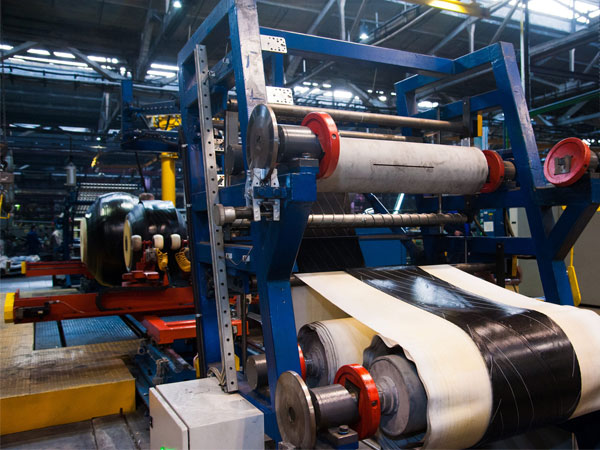 Industrial machine wrapping large rolls of black and white material inside a factory setting.