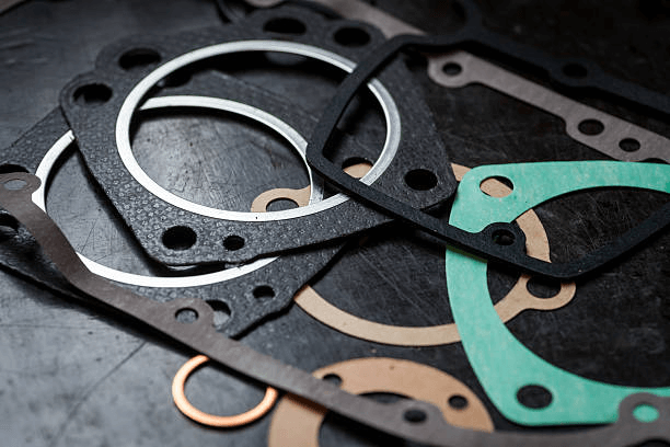 Various automotive gaskets of different shapes and materials laid out on a dark surface.