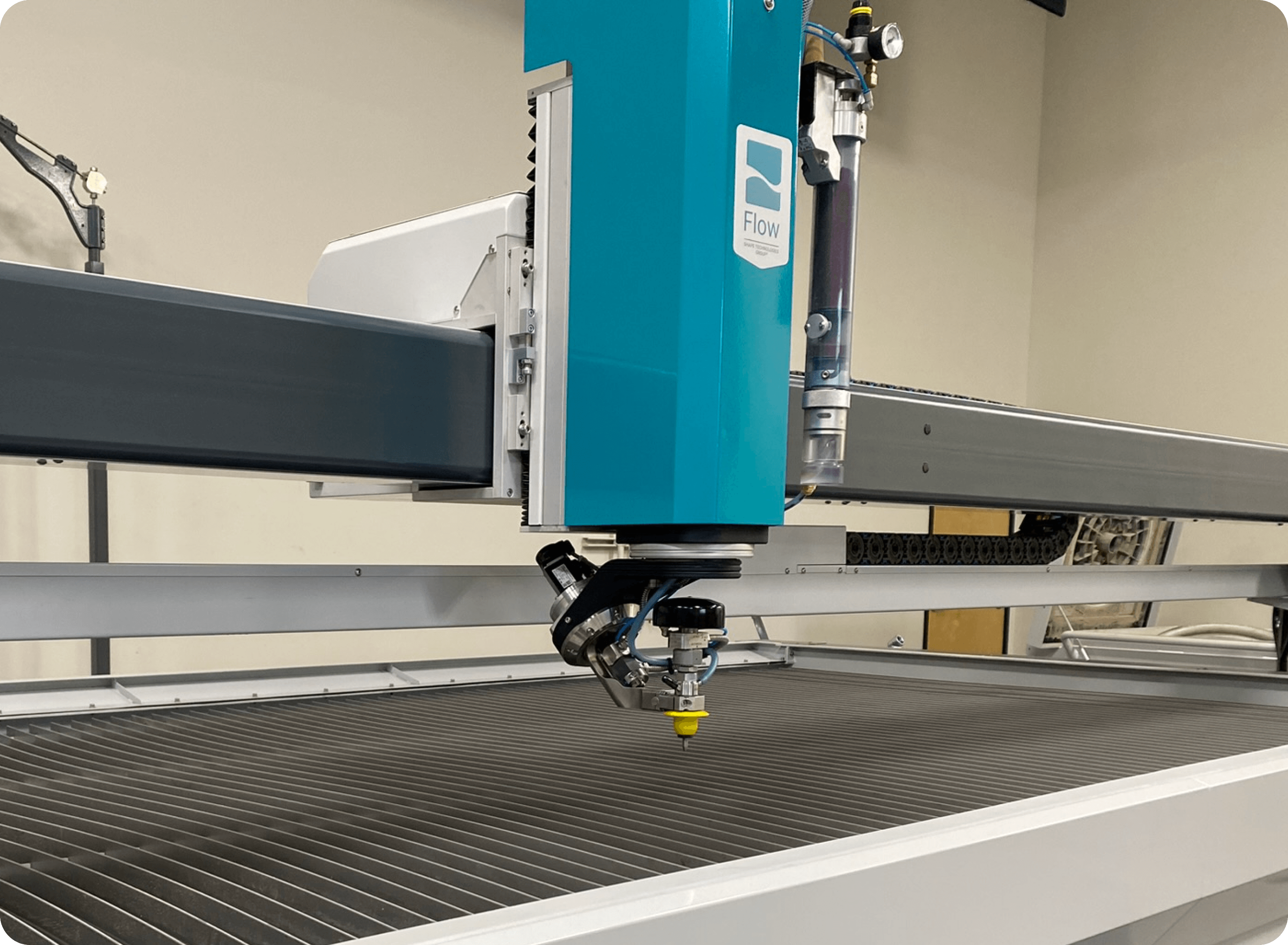 Close-up of a Flow waterjet cutting machine with blue and gray components in an industrial setting.
