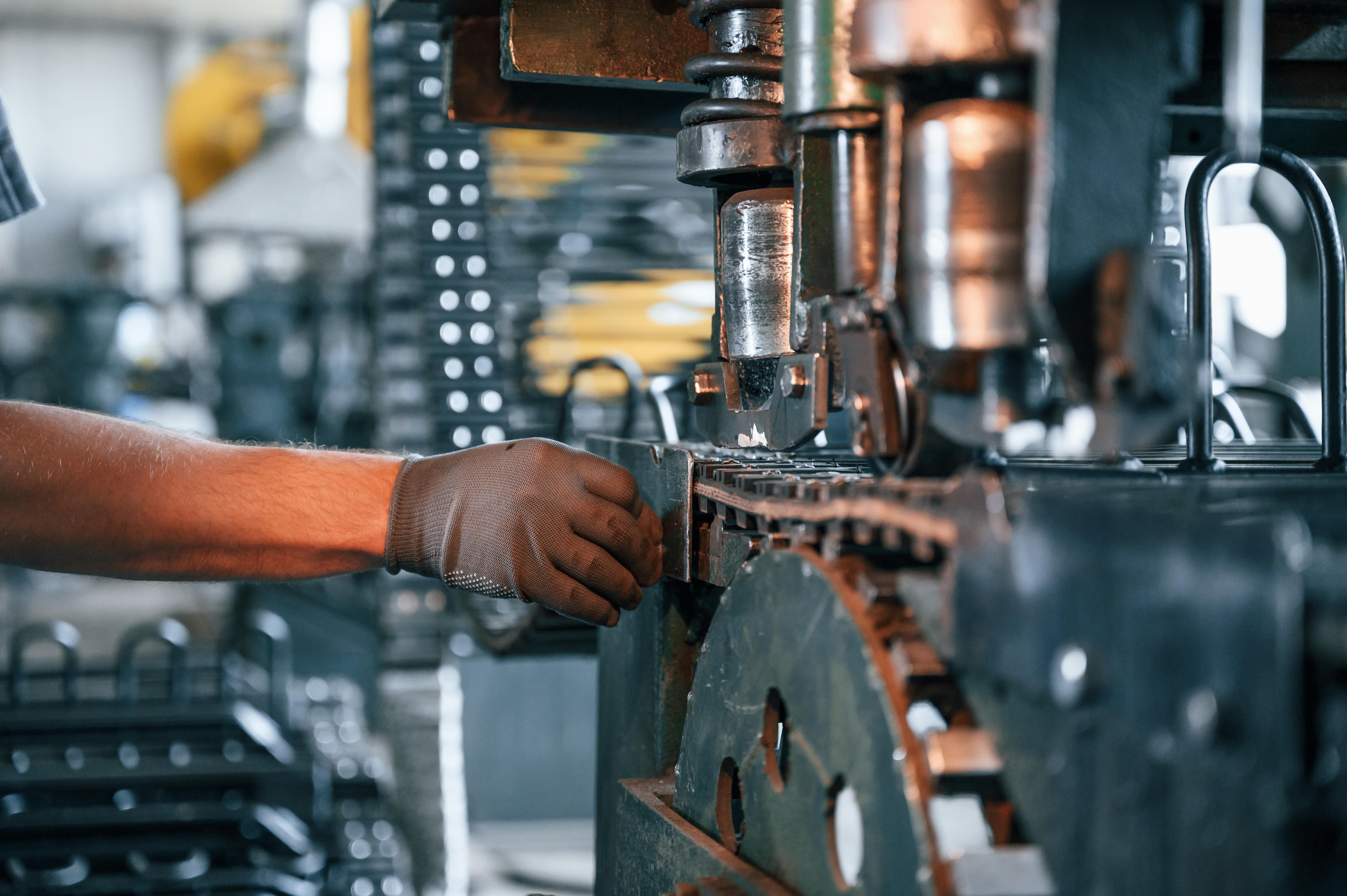 Worker wearing a glove operating a heavy industrial machine with large gears and chains in a manufacturing setting.
