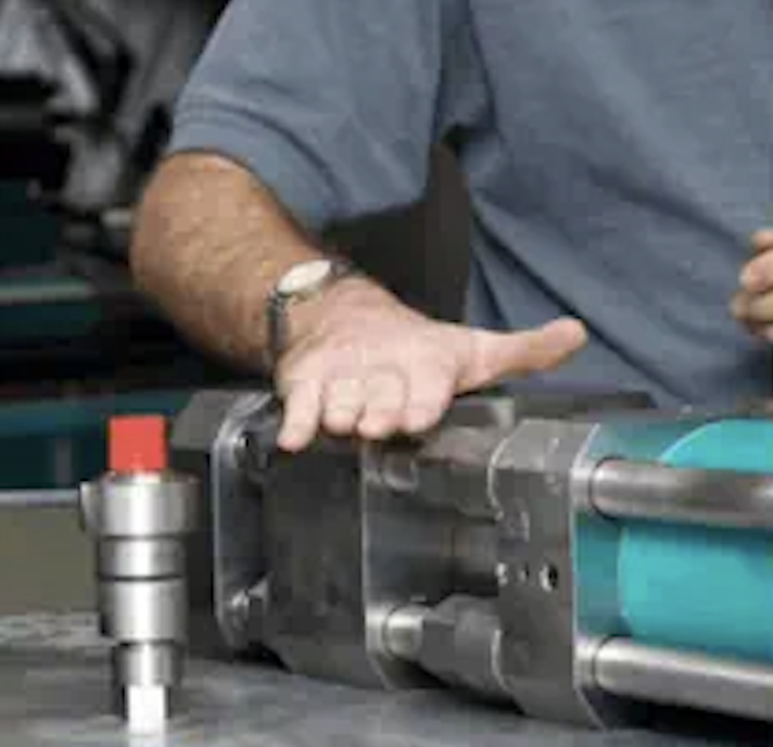 Person wearing a watch handling a large industrial metal tool or machine part with a blue component on a workbench.