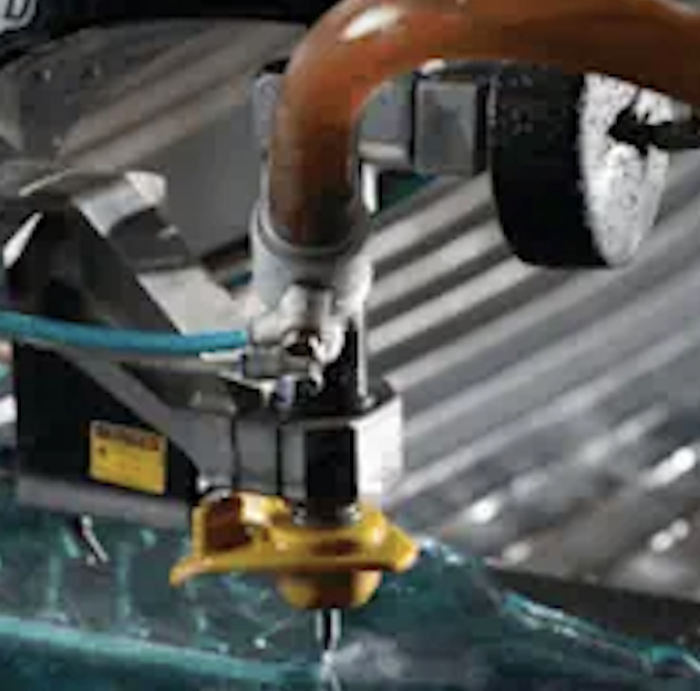 Close-up of an industrial CNC cutting machine with a rotating tool working on a green material.