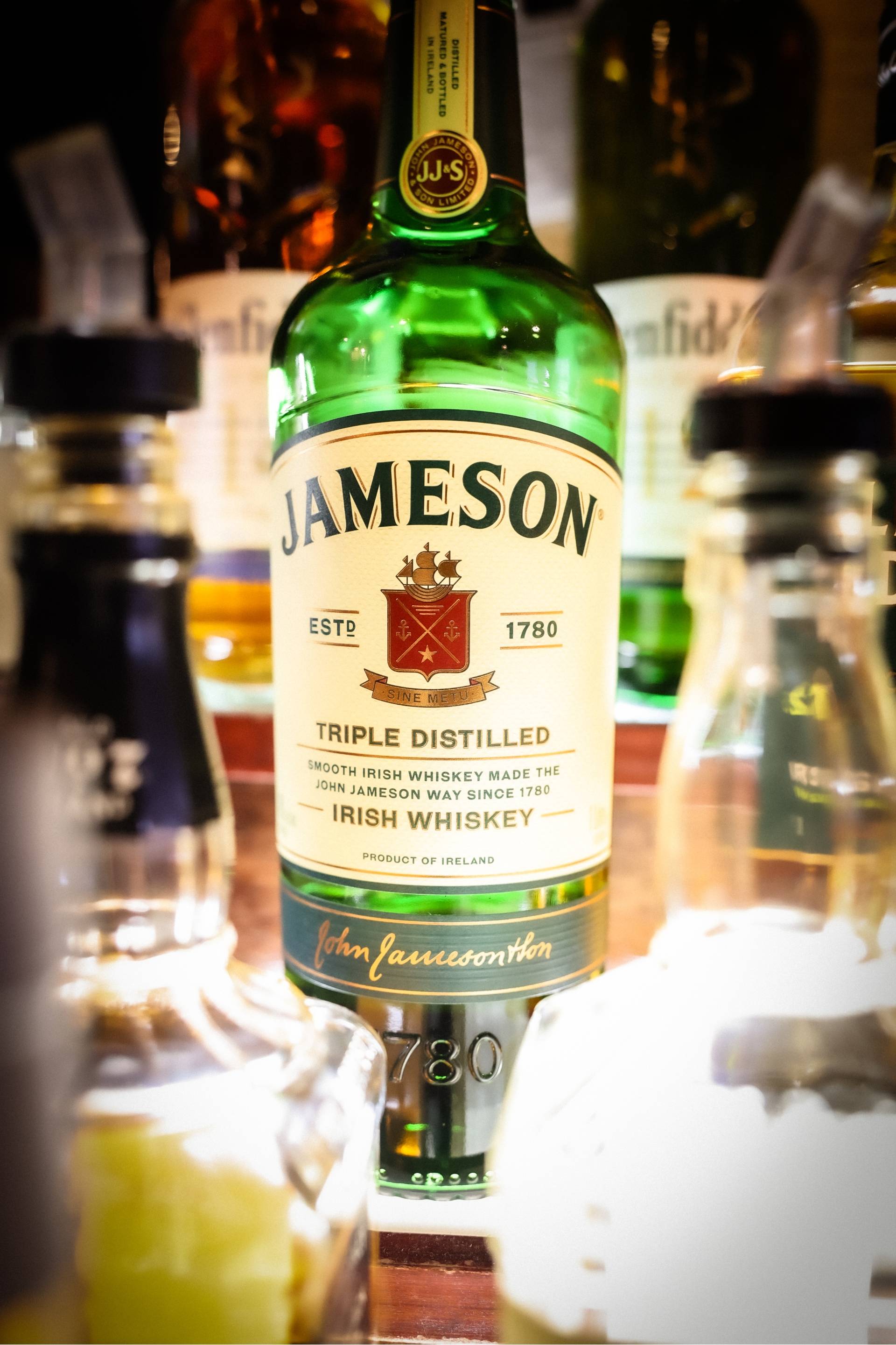 Close-up of a green bottle of Jameson Irish Whiskey with other blurred bottles in the background.
