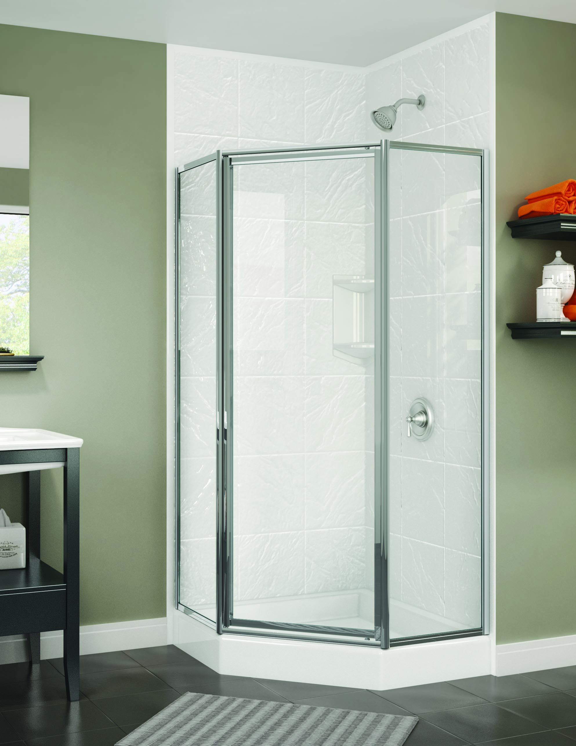 Modern corner shower with a neo-angle glass door and textured white tile walls. The shower features a chrome showerhead and built-in corner shelving. The surrounding bathroom has olive-green walls, dark flooring, and a floating shelf with orange towels and glass accessories for a pop of color.