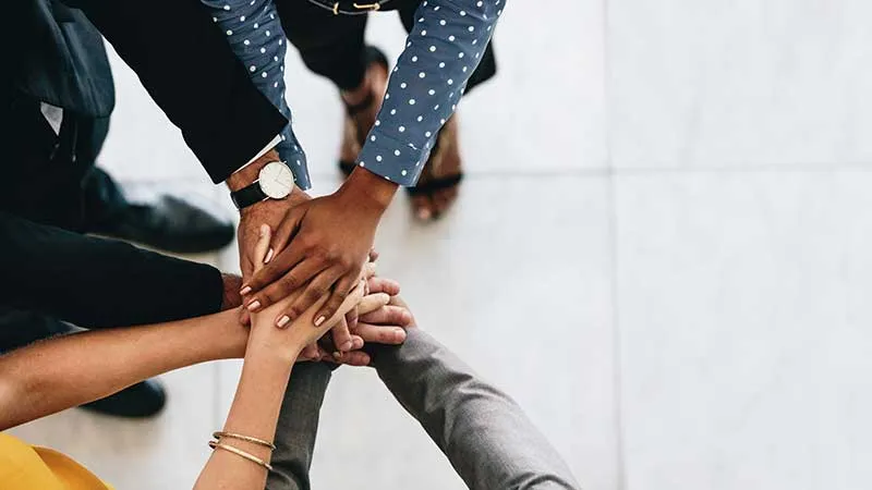 A team in a huddle with stacked hands #HowYouLive