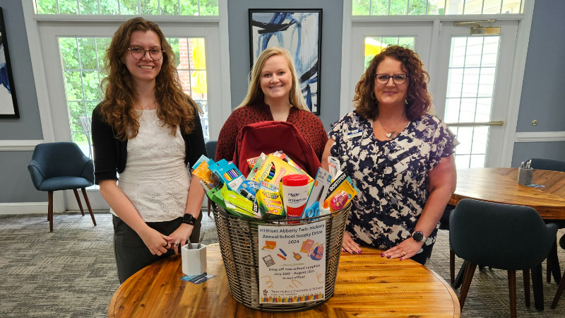 Three employee women standing around a supply basket.
