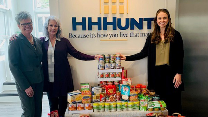 Three Ladies standing around a table of food donations