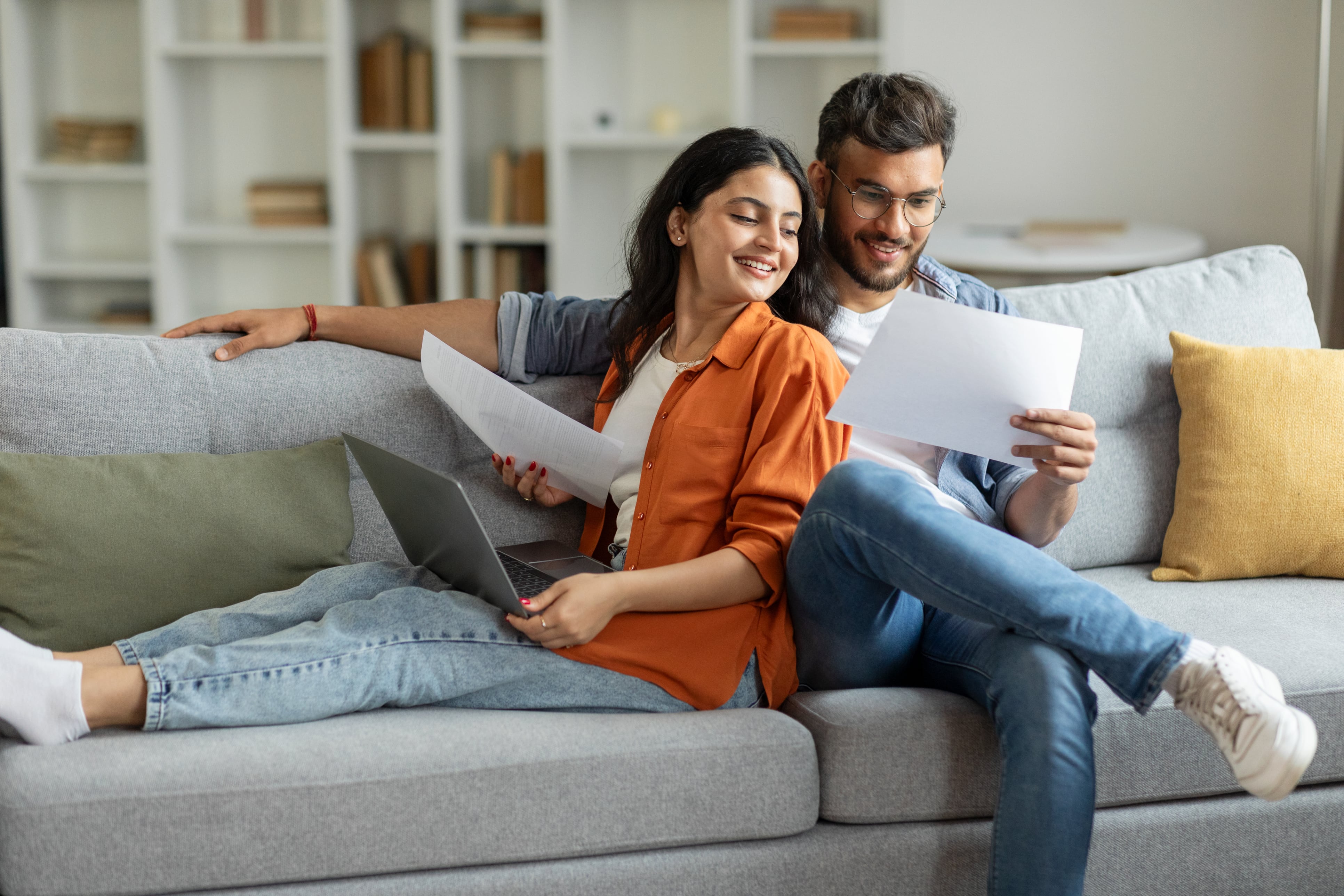 A couple sitting on couch reviewing bills, looking happy.
