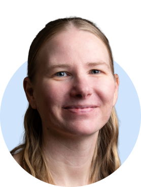 Smiling person with long blonde hair and blue-framed glasses