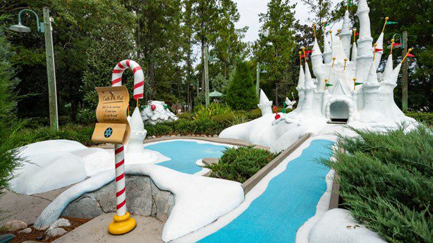 A whimsical landscape featuring a snowy castle, whimsical pathways, and candy cane signage amidst lush greenery.