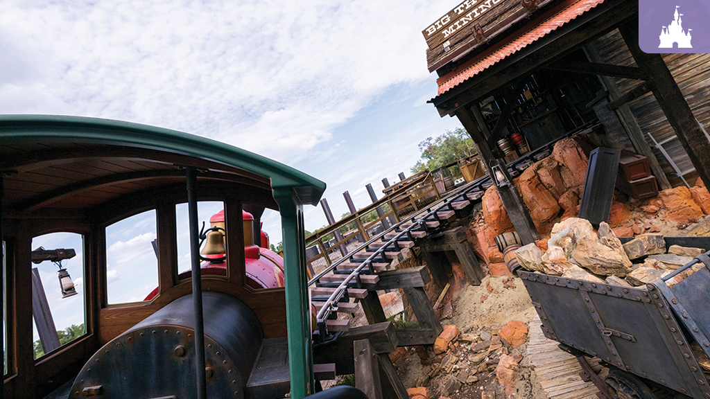 Thunder Mountain Railroad train on the track at Magic Kingdom, passing rustic mining structures and rocky terrain at Disney World