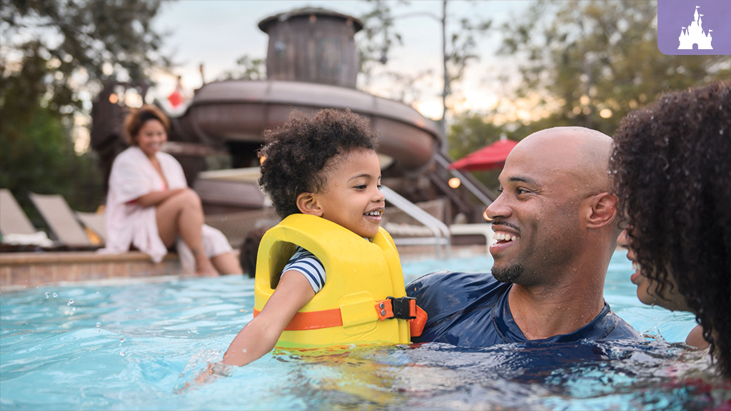 Family enjoys the Meadow Swimmin' Pool at Fort Wilderness, with the corkscrew waterslide visible in the background.