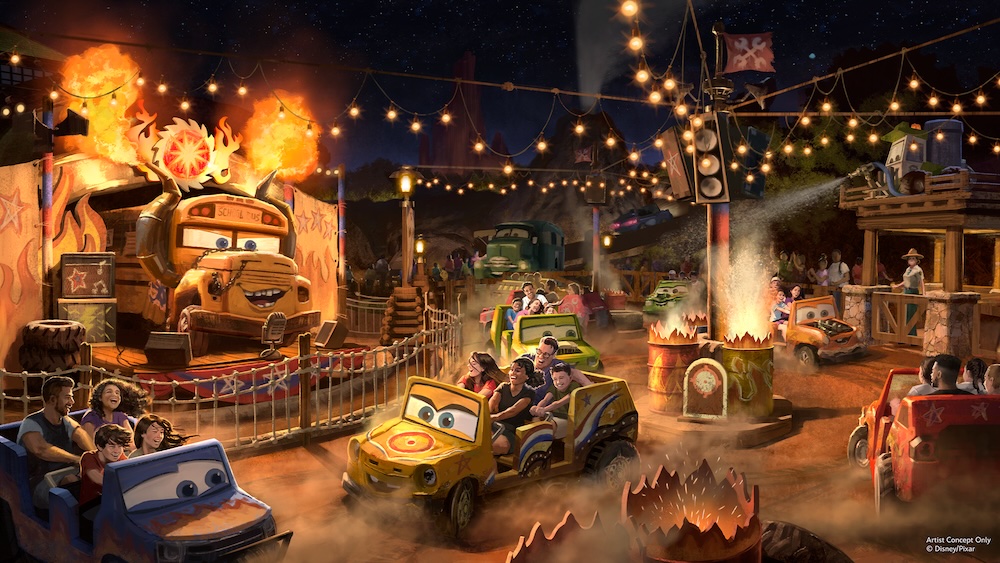 Cars-themed ride area at night with riders in spinning car vehicles around fire-lit barrels and an animatronic bus on stage under string lights