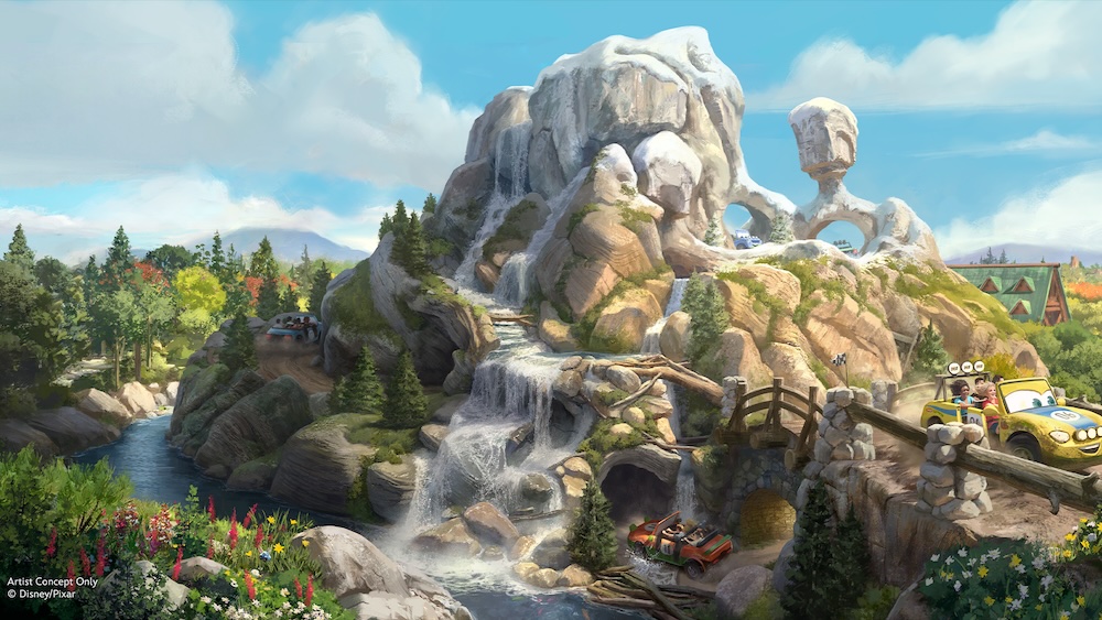 Rocky mountain with waterfalls and a forested river, small ride vehicles with smiling cartoon faces carrying passengers along a bridge and track.
