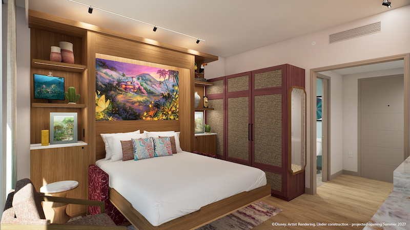 Modern hotel bedroom with king bed under tropical painting, built-in wooden shelves, cushions, closet, armchair and open bathroom door