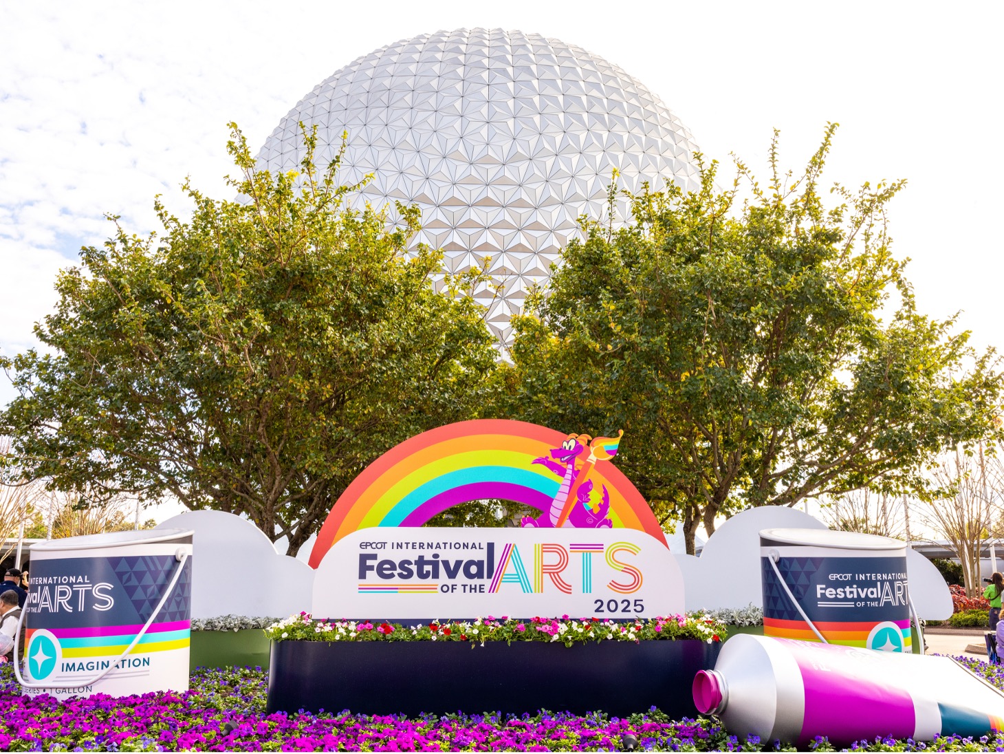 Display featuring a rainbow arch and a cartoon dragon holding a paintbrush in front of the geodesic sphere, with oversized paint tubes and purple flowers.