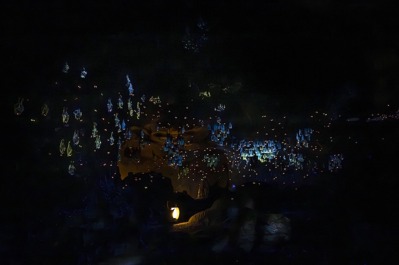Dark cavern interior illuminated by hundreds of small blue and yellow hanging lanterns and a single ground-level lamp