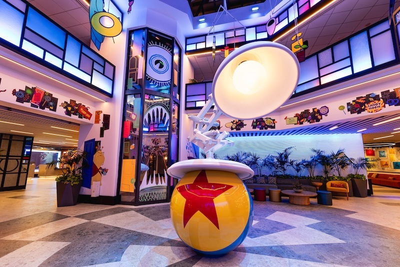 Lobby with a large white adjustable lamp perched on a yellow ball with red star, colorful murals and seating areas in the background.