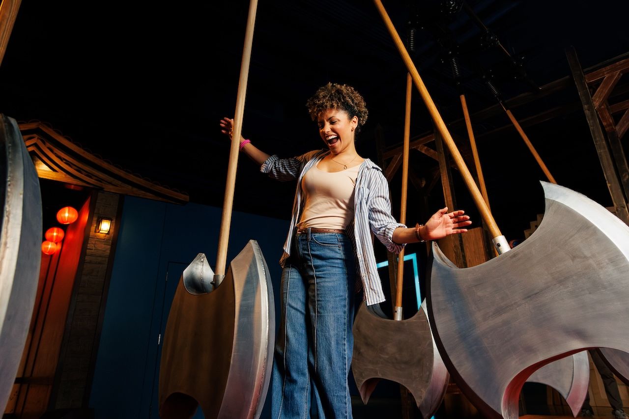 Woman standing among large curved metal sculptures in a dimly lit indoor exhibit.