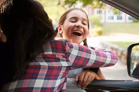 Young girl hugging her mother through a car window