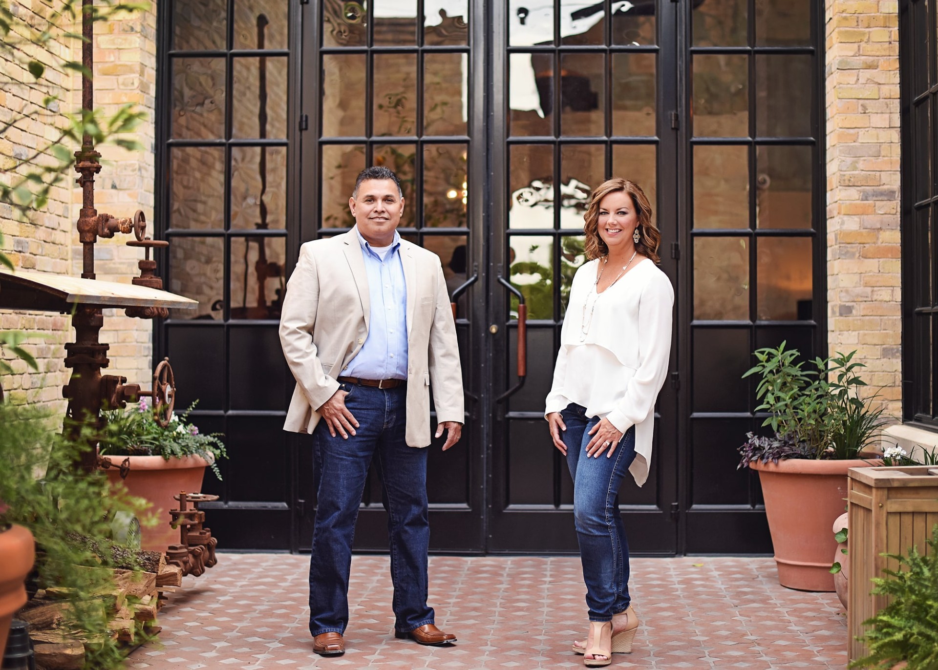 Jana and Armando in front of black-framed windows and brick wall