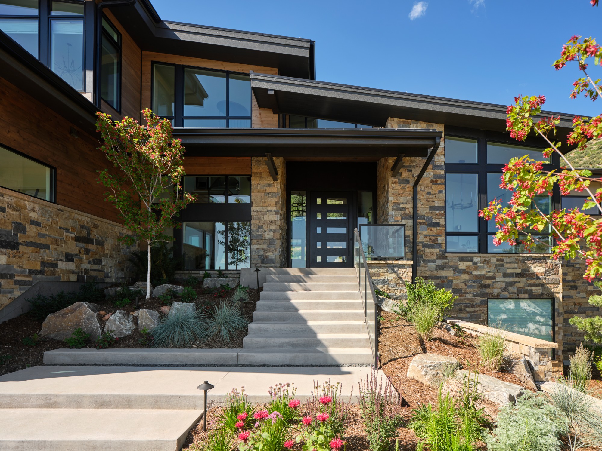 Modern stone and wood home with glass entry and landscaped front yard