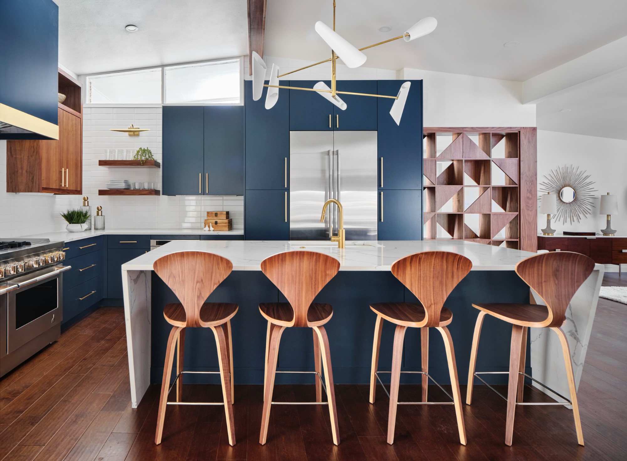 Modern kitchen with blue cabinets, wooden bar stools, and geometric pendant light