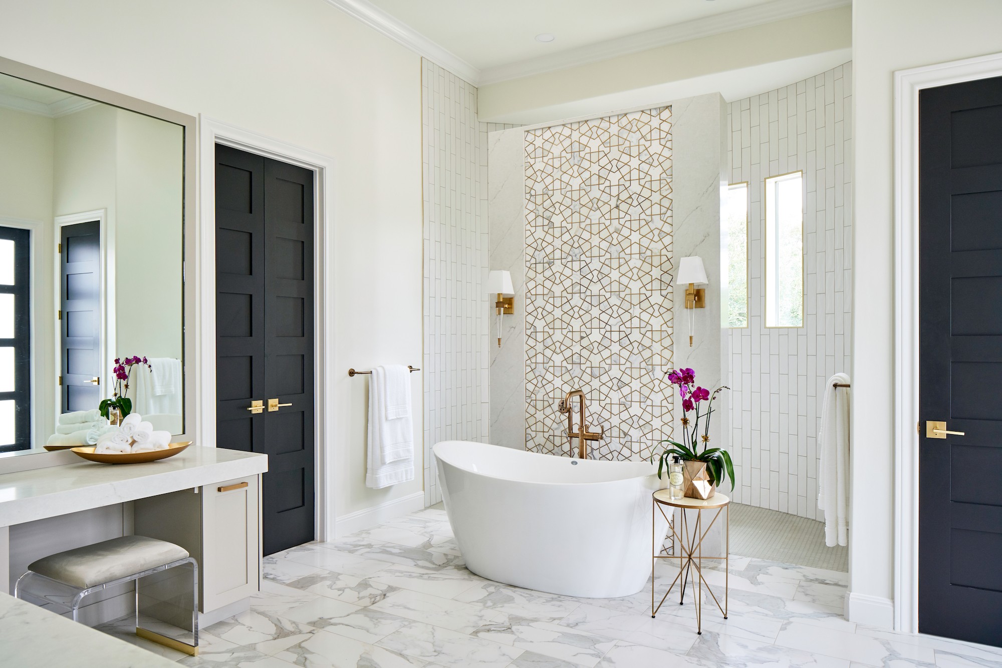 Elegant white bathroom with freestanding tub, geometric tile, and orchids