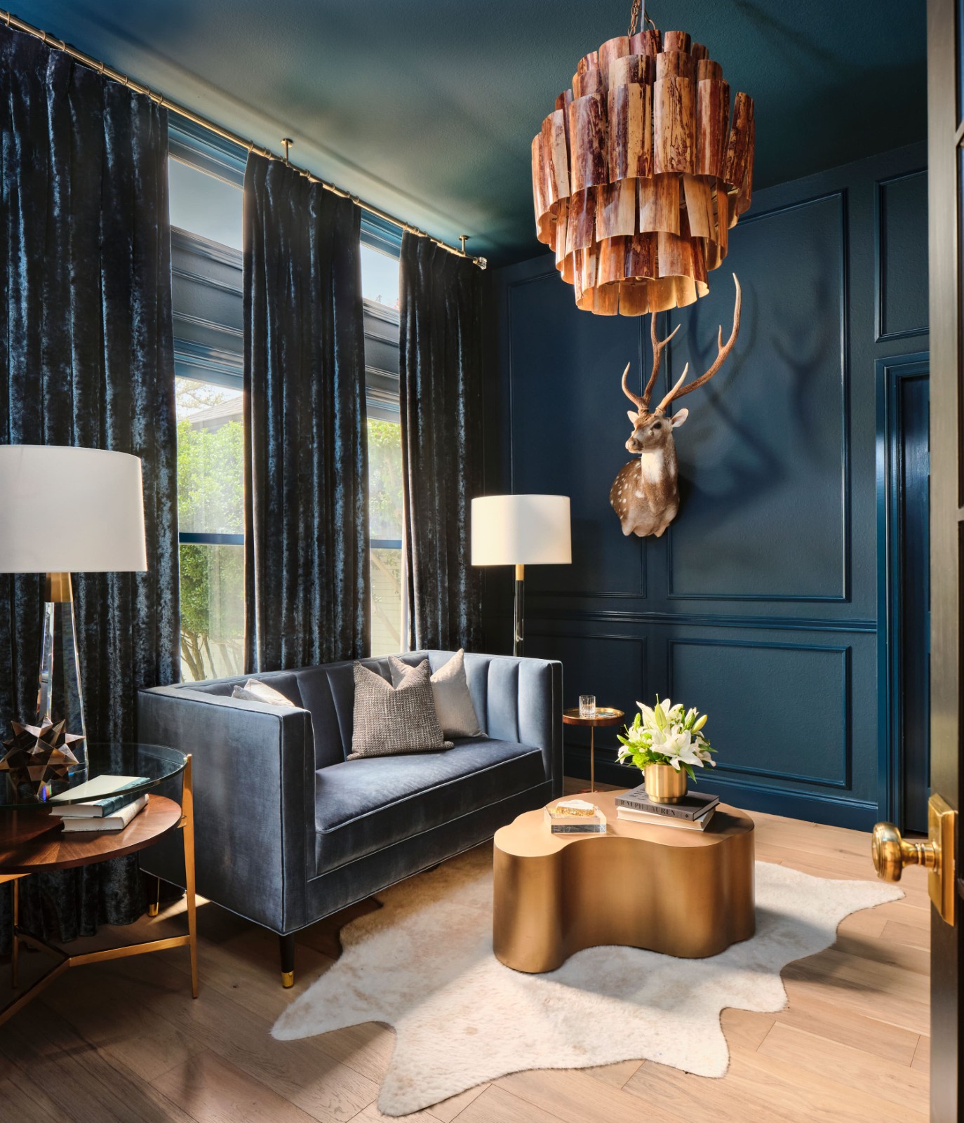 Elegant blue room with deer head, gold coffee table, and wooden chandelier