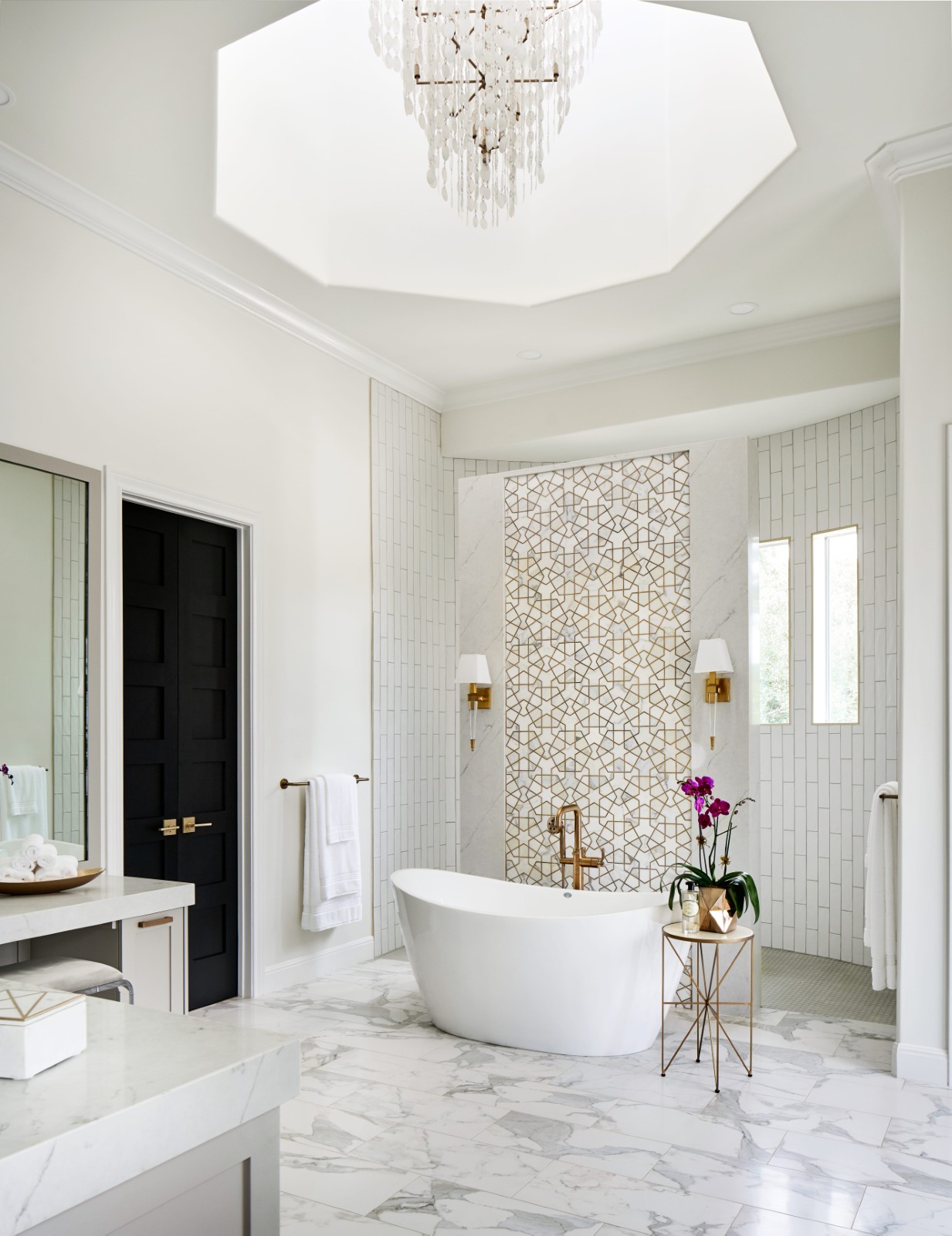 Luxurious white bathroom with freestanding tub, chandelier, and geometric tile