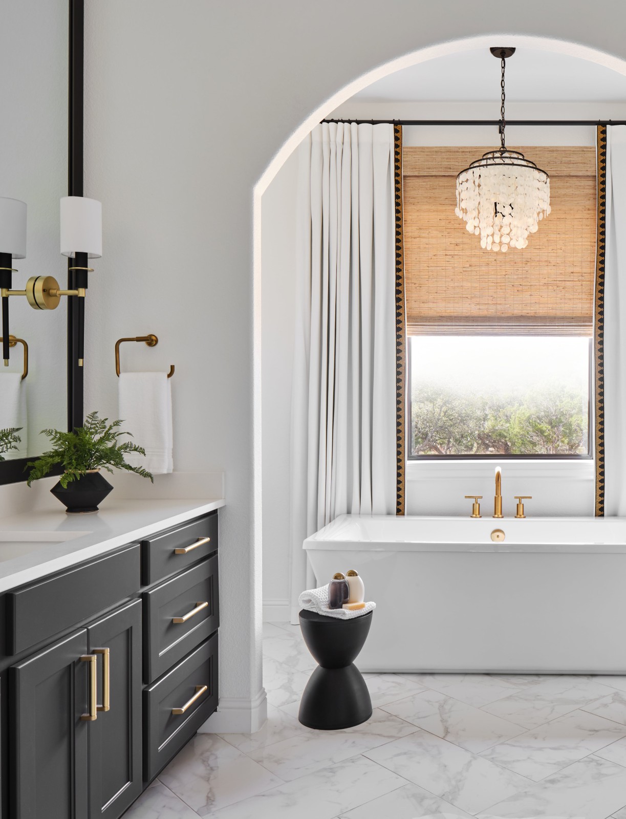Elegant bathroom with white tub, black vanity, and capiz shell chandelier