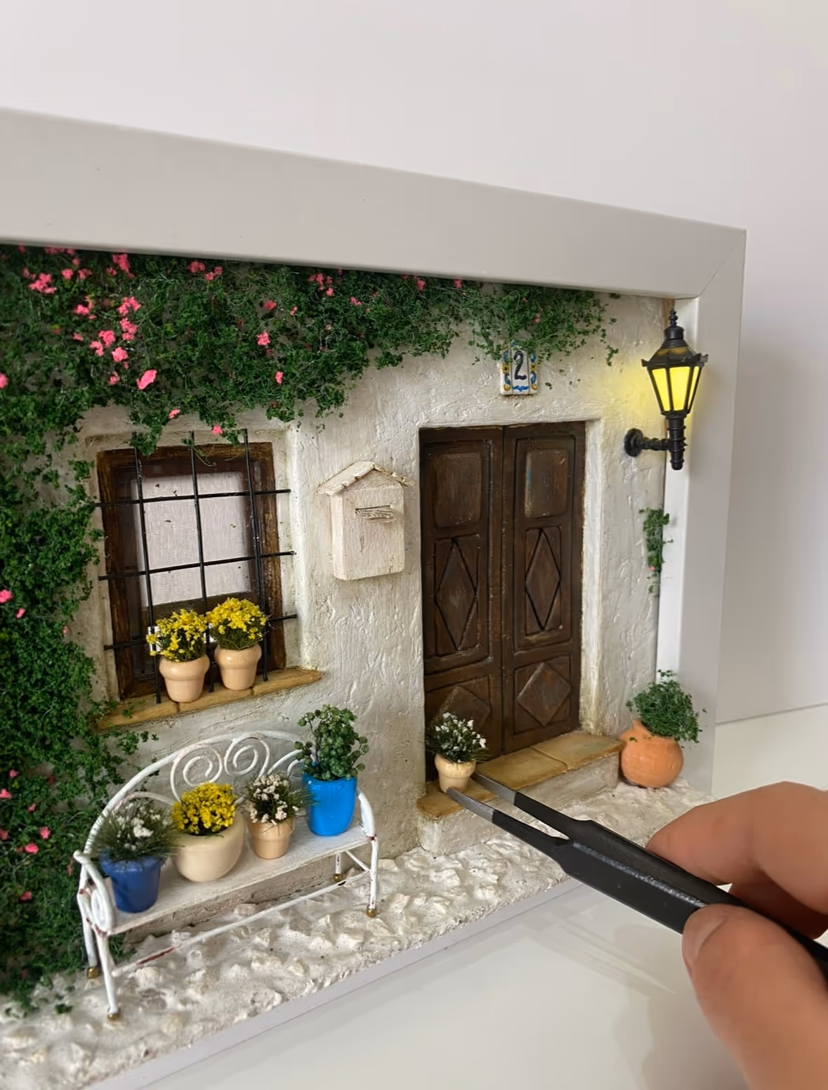 Close-up of Rachel using tweezers to place a tiny plant on a finished miniature building facade.