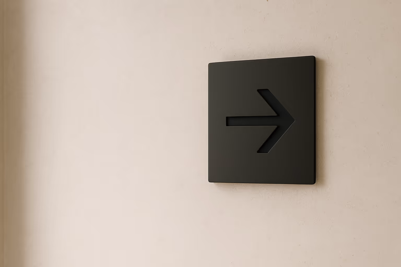 Minimal matte-black arrow wall plate on a light stone surface
