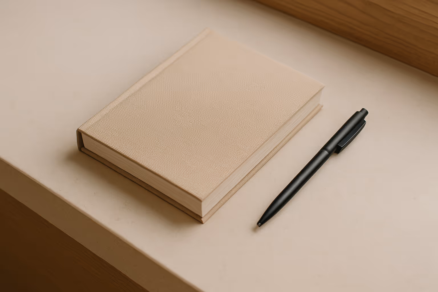 Beige linen notebook with matte black pen on light stone desk