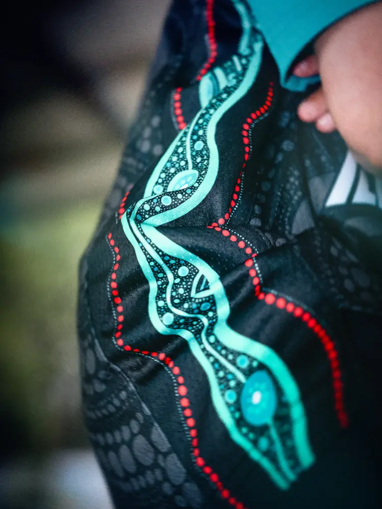 Close-up of the jersey artwork: a teal line with red dot work running over a pattern of grey dots on the black jersey.
