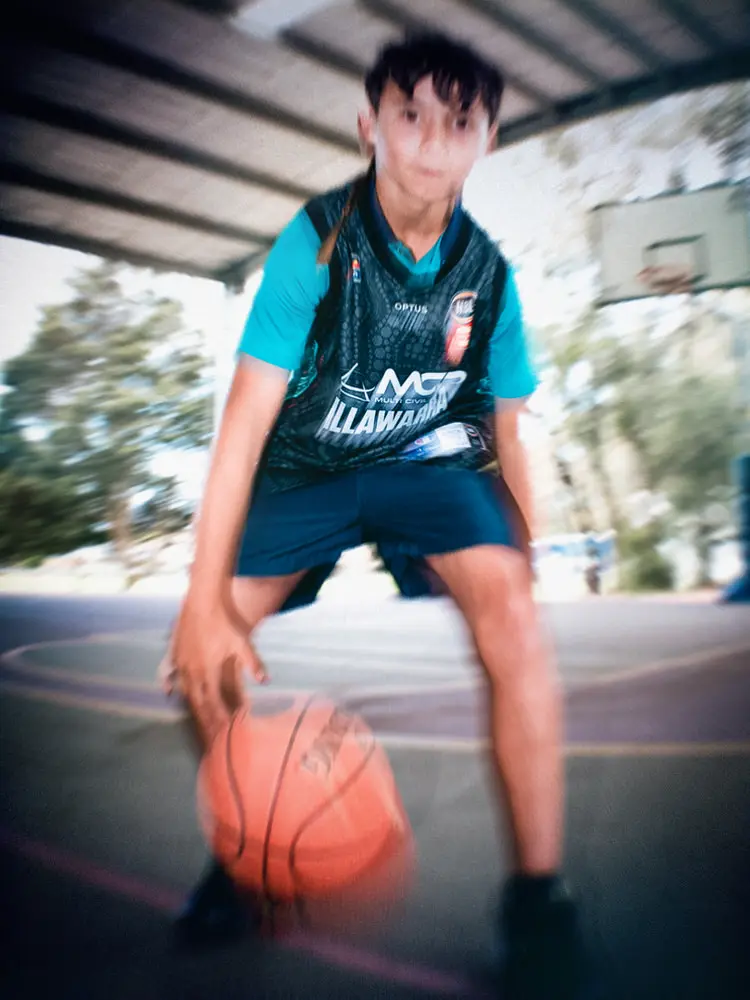 A participant crouches low and dribbles a basketball towards the camera on an outdoor court.