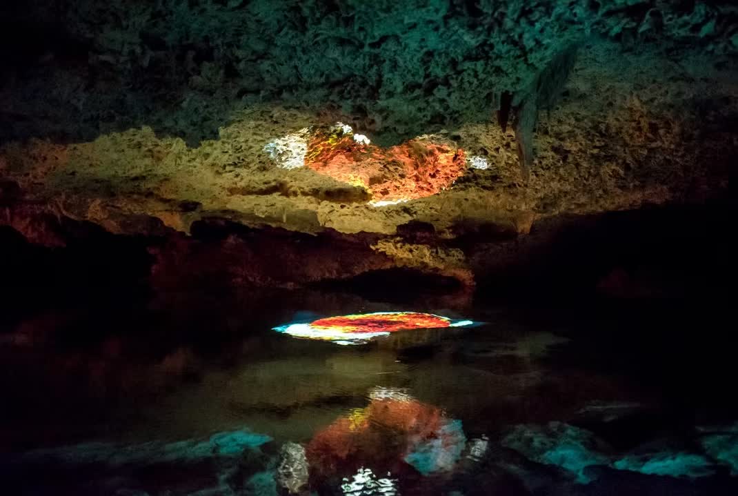 Interior of a dark underwater cave with colorful light reflecting on the water surface.